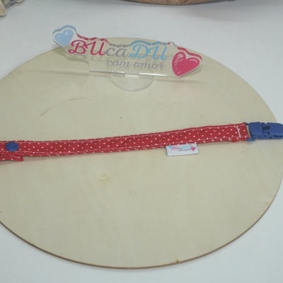 Tira vermelha com pontos brancos e fecho azul sobre placa de madeira clara