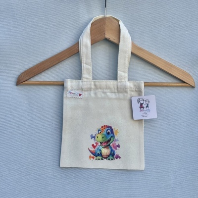 Saco de tecido creme com ilustração de dinossauro colorido e etiquetas visíveis