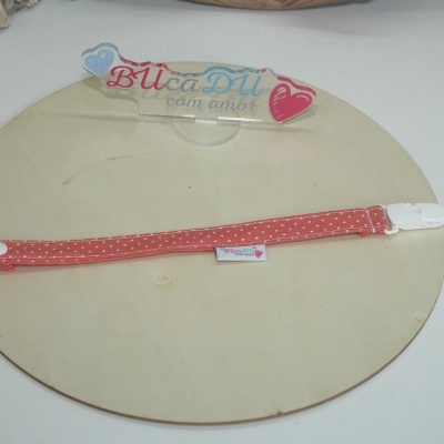 Fita de tecido cor-de-rosa com pontos brancos e fecho branco sobre base de madeira