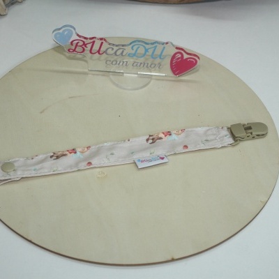 Tira de tecido estampado com clip de plástico e botão, sobre placa circular de madeira clara