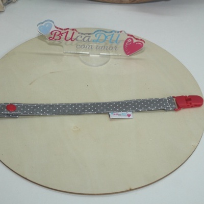 Fita cinzenta com bolinhas brancas e fecho vermelho sobre base redonda de madeira