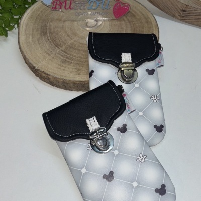 Duas bolsas de padrão cinza com fechos metálicos sobre mesa branca perto de planta e placa de madeira