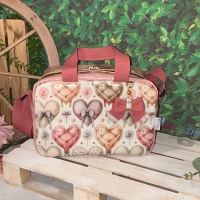 Bolsa com padrão de corações e laço cor de rosa sobre palete de madeira clara e fundo de folhas verdes