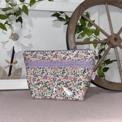 Necessaire estampada com padrão de folhas coloridas sobre pano rosa com decoração de parede