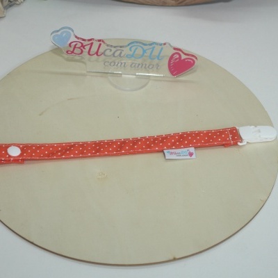 Presilha de tecido vermelho com bolinhas brancas e fecho branco sobre base de madeira redonda