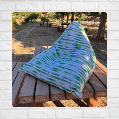 Pufe de tecido listrado verde e branco numa mesa de madeira ao ar livre