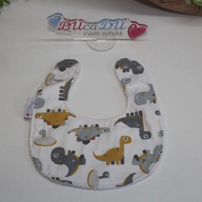 Babete branco com padrão de dinossauros cinza e amarelos e etiqueta BUcaDU com amor