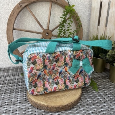 Bolsa colorida com padrão de aves e flores, alça turquesa e laço decorativo