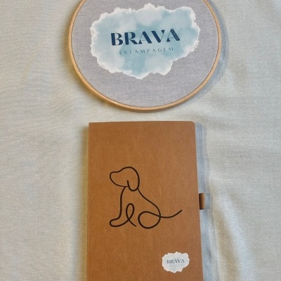 Caderno castanho com desenho de cão e bastidor de madeira com tecido e texto BRAVA ESTAMPAGEM