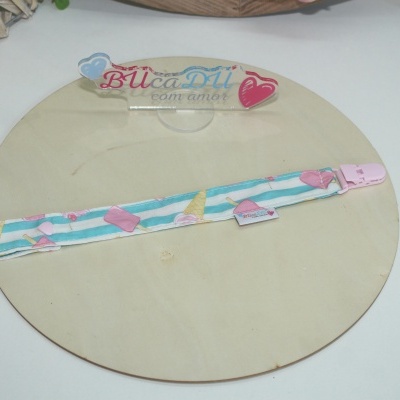 Tira de tecido azul claro com estampado de gelados cor-de-rosa e fecho cor-de-rosa sobre superfície de madeira clara
