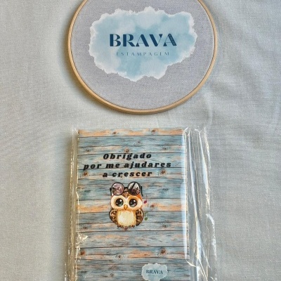 Caderno com capa azul claro decorada com ilustração de coruja e texto em português, embalado em plástico