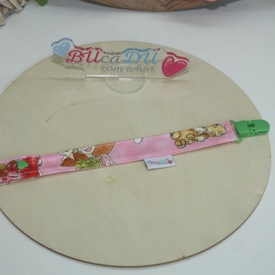 Clipe para chucha rosa com estampa de ursos e fecho verde sobre superfície redonda de madeira