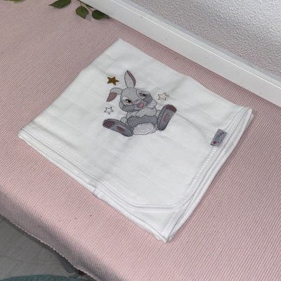 Manta branca de tecido com bordado de coelho e estrelas sobre superfície rosa