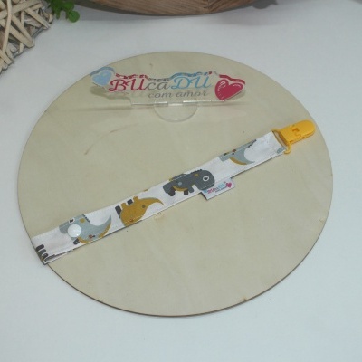 Fita para chupeta em tecido branco com padrão de elefantes e fecho amarelo sobre base redonda de madeira