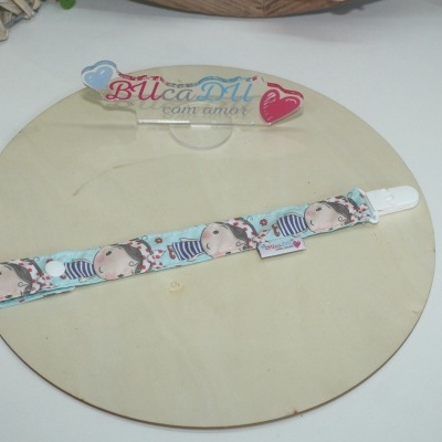 Fita de tecido azul com estampa de menina e clipe branco sobre base redonda de madeira e placa com texto
