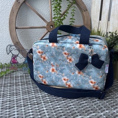 Mala azul claro com padrão floral e alças azuis escuro sobre superfície de rattan com decoração de madeira e plantas