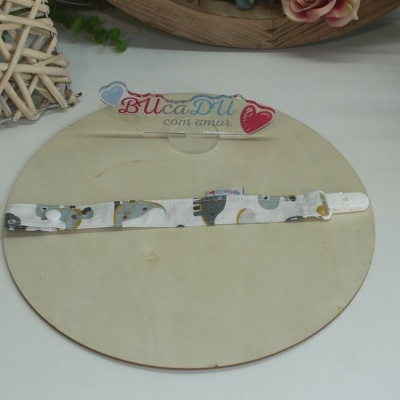 Prendedor de chupeta em tecido branco com padrão de animais cinzentos, azul e amarelo sobre base redonda de madeira clara.