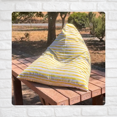 Pufe amarelo com riscas brancas sobre mesa de madeira ao ar livre