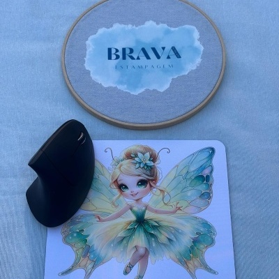 Rato vertical preto sobre tapete de rato com fada colorida e bastidor com tecido azul claro e texto BRAVA ESTAMPAGEM