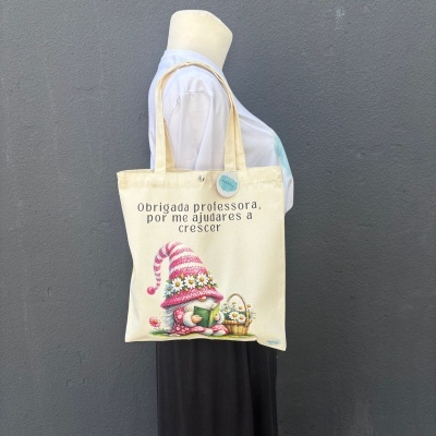 Saco de tecido creme com texto e ilustração de gnomo a ler e cesto de flores