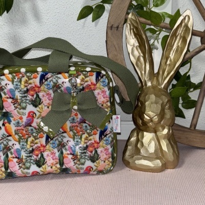 Bolsa colorida de pássaros com laço verde e estatueta dourada de coelho ao lado
