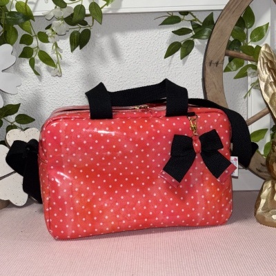 Mala vermelha com bolinhas brancas e laço preto sobre tecido rosa