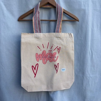 Mala de pano bege com texto e corações e alças listradas coloridas