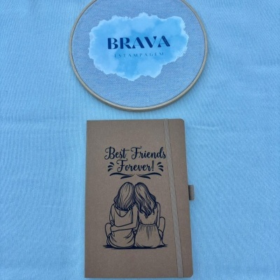 Caderno castanho com ilustração e texto e bastidor de bordado com logotipo BRAVA ESTAMPAGEM