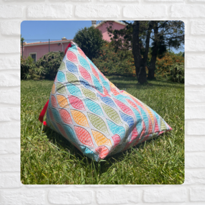 Puff triangular colorido com padrão de folhas sobre relva