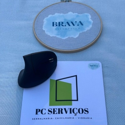 Rato ergonómico preto com tapete de rato branco e bastidor de bordado em fundo azul-claro.