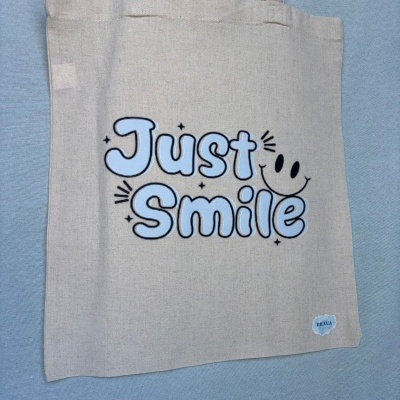 Saco de tecido bege com texto colorido e rosto sorridente