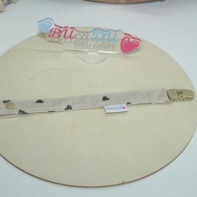 Prendedor de tecido bege com corações pretos e mola de pressão em base de madeira.