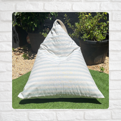 Pufe triangular riscado azul e branco em relva artificial junto a vasos com plantas