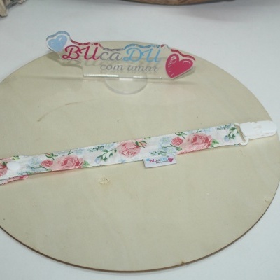 Prendedor de chupeta floral rosa com fecho branco sobre placa de madeira