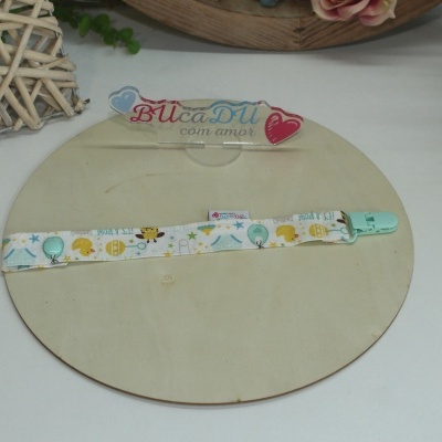 Prendedor de chupeta tecido colorido com clips azul claro sobre base circular madeira.