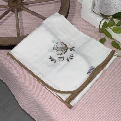 Manta branca com borda castanha e bordado de balão de ar quente e avião