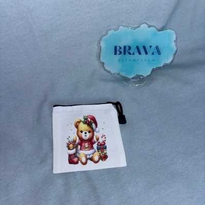 Bolsa branca com estampa de urso de pelúcia natalício e placa azul com texto BRAVA ESTAMPAGEM