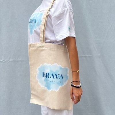 Pessoa com t-shirt branca e sacola de tecido BEGE com estampa azul BRAVA ESTAMPAGEM