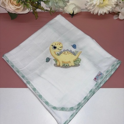 Fralda branca com bordado de dinossauro amarelo e borboletas, borda xadrez verde claro.