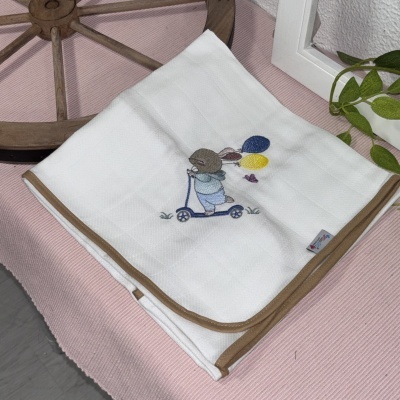 Toalha branca de bebé com bordado colorido e borda castanha sobre tecido rosa.