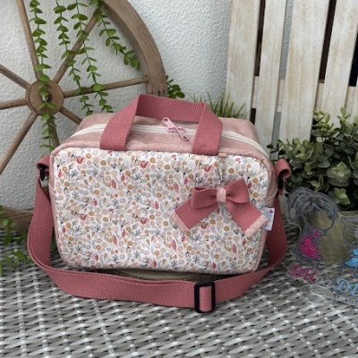 Mala floral rosa com alças e laço decorativo sobre superfície de rattan