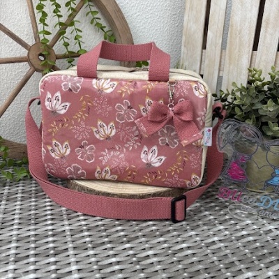 Bolsa retangular cor-de-rosa com padrão floral, laço pendurado e alças sobre mesa de rattan cinza