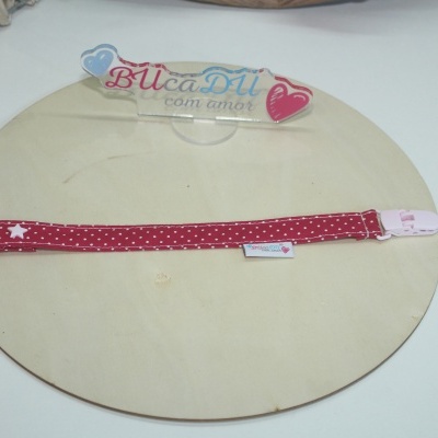 Tira vermelha de tecido com pontos e fecho plástico rosa sobre placa de madeira