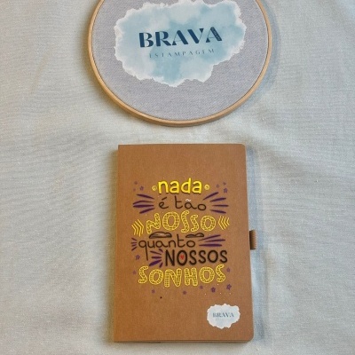 Caderno castanho com frase decorativa e aro de bordado com tecido cinza e marca BRAVA