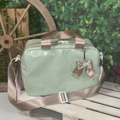 Mala verde-claro com pontos brancos e alças douradas sobre pallet com fundo de folhas verdes