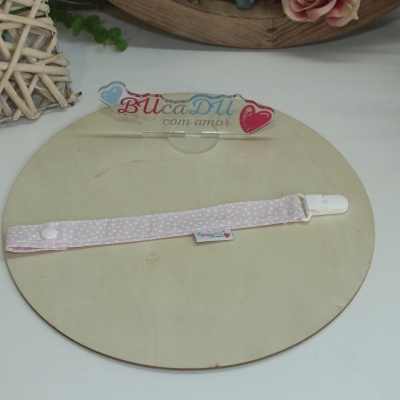 Prendedor de chucha rosa com pontos brancos e clip branco sobre base redonda de madeira clara