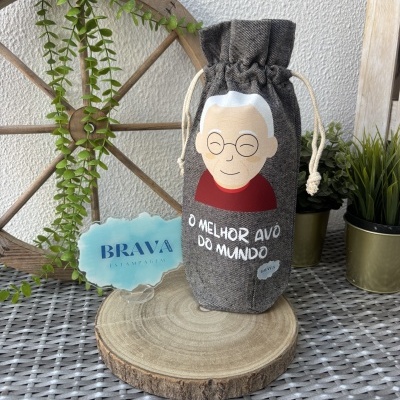 Saco de tecido com desenho de avô e texto O MELHOR AVÔ DO MUNDO sobre base de madeira e plantas