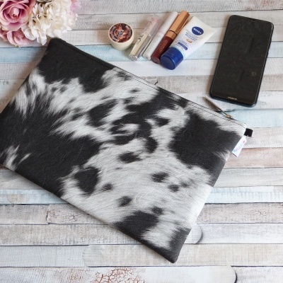 Bolsa em tecido preto e branco com padrão abstrato, flores, telemóvel e cosméticos em fundo de madeira clara