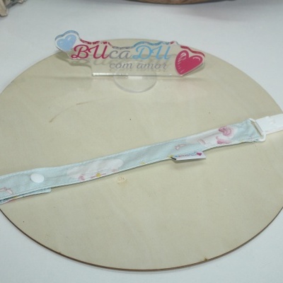 Tira para prender chupeta azul claro estampada sobre base redonda de madeira