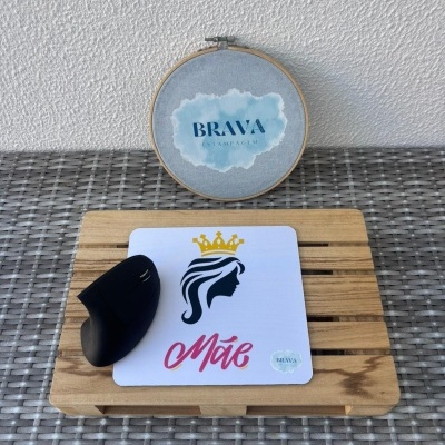 Tapete de rato branco com ilustração de mulher e texto, rato preto, base de madeira e bordado azul na parede